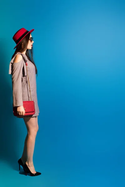 Szép modell a divatos piros kalap és egy piros kuplung a kék háttér. — Stock Fotó