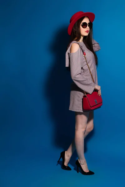 ファッショナブルな赤い帽子と青い背景の赤いクラッチで素敵なモデル. — ストック写真