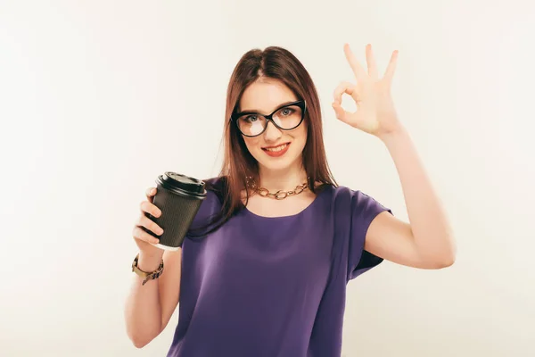 Giovane bella ragazza in bicchieri con tazza di caffè da un fast food sorridente su uno sfondo grigio. gesti delle mani . — Foto Stock