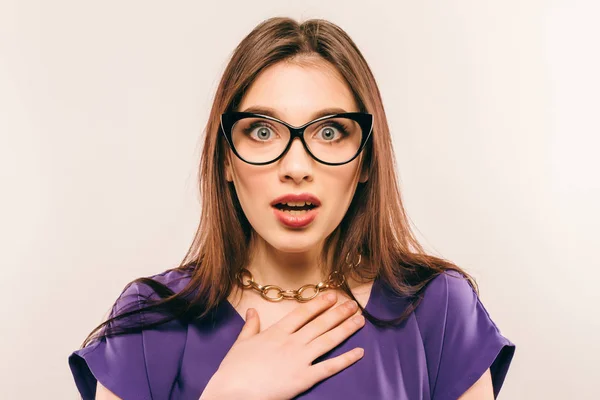 Joven hermosa mujer con expresión facial de sorpresa de pie sobre fondo gris. Llevar en vestido de moda y gafas. Mirando a la cámara —  Fotos de Stock