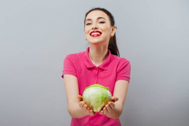 Çiğ gıda, sebze kavramı. Kırmızı lahana gri arka plan üzerinde onun elinde tutan casual giyim gülümseyen iyi görünümlü kız portresi. Sağlıklı cilt, parlak kahverengi saçlı. Portre. Stüdyo vurdu.