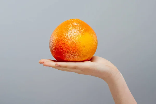 Vacaciones de verano. Cítricos de pomelo con paja para beber en mano femenina sobre gris. Comida y bebida saludables — Foto de Stock