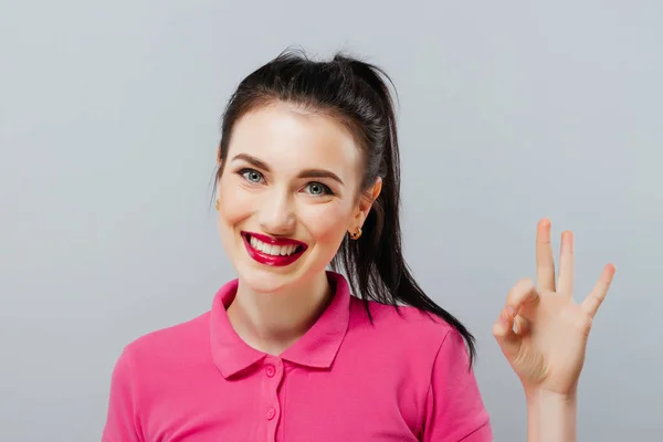 Hermosa mujer joven con el pelo largo y rizado marrón en mini vestido rosa posando con la mano en la cadera y mostrando signo ok — Foto de Stock