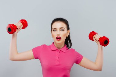 Gri arka plan üzerinde iki dumbbells ile oynayan genç güzel kadın