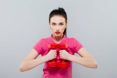 İki plastik dambıl tutan genç bir kız. Gri arka planı.