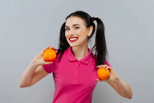 Привлекательная улыбающаяся молодая женщина позирует с двумя свежими апельсинами на белом фоне — стоковое фото