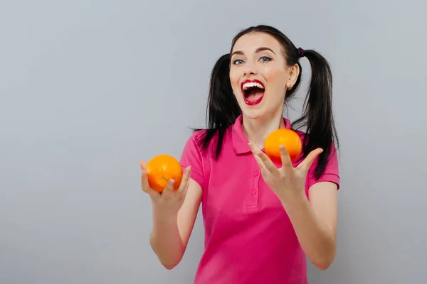 Mujer con el pelo largo y liso, sosteniendo dos naranjas, mirando hacia arriba fondo gris — Foto de Stock