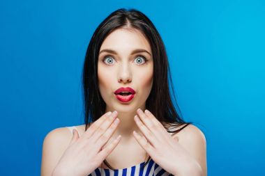 Sürpriz genç güzel kız mavi arka plan üzerinde izole kamera bakıyor