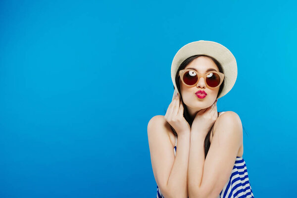 Cheerful beautiful girl in hat and sun glasses. Smiling widely, looking and pointing aside. Summer outfit. Waist up, studio, indoors