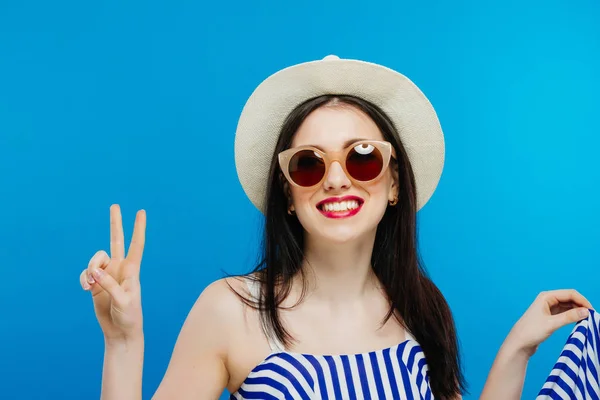 Brunette fille avec des lunettes de soleil et chapeau sur fond bleu . — Photo