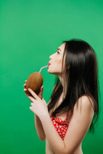 Retrato de una mujer bonita con el pelo largo y oscuro en traje de baño brillante Beber cóctel tropical sobre fondo verde en el estudio . — Foto de Stock