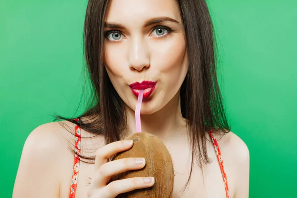 Primer plano Retrato de modelo femenino alegre Beber cóctel en coco sobre fondo verde en el estudio . — Foto de Stock