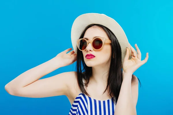 Portrait de modèle féminin dans les lunettes de soleil de mode et chapeau d'été sur fond bleu . — Photo