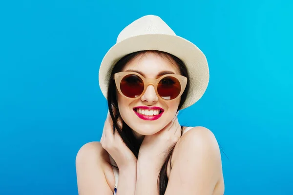 Портрет улыбающейся модели в модных солнцезащитных очках и летней шляпе на голубом фоне . — стоковое фото