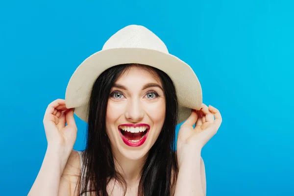 Ritratto di bruna sorridente che indossa un cappello estivo in posa in studio su sfondo blu . — Foto Stock