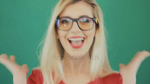 Bionda carina in occhiali di moda smorfia su sfondo verde in studio. Primo piano Ritratto di giovane donna sorpresa con labbra sensuali rosse . — Video Stock