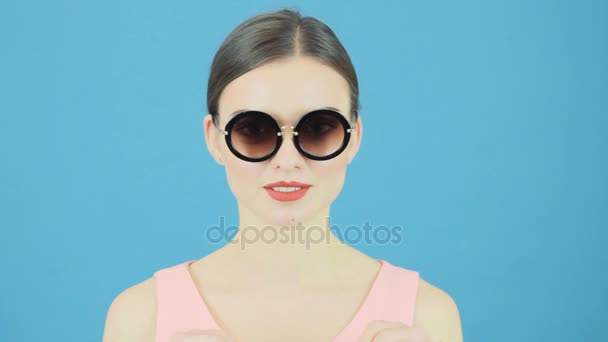Retrato de belleza de una mujer morena con gafas de sol frescas sosteniendo una bolsa de compras rosa sobre fondo azul en el estudio. Concepto de venta estacional . — Vídeo de stock