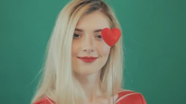 Uzun saç ve kırmızı dudaklar kutluyor Valentines gün genç sevimli kız closeup portresi. Sarışın yeşil arka planda Studio ellerinde küçük kalp ile şaşırtıcı. Tatil kavramı.