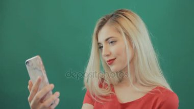 Gülümseyen sarışın kadın alarak Selfie yanında Studio yeşil zemin üzerine Her Smartphone olduğunu. Genç ve güzel kız kendini mobil kullanarak çekim portre portre.