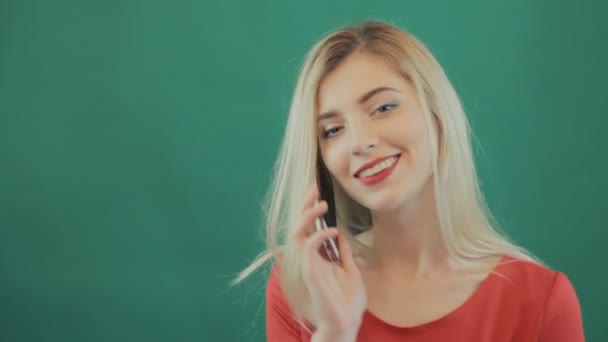 Mujer insatisfecha no puede llamar a alguien por teléfono inteligente. Retrato de una joven rubia con el pelo largo, labios sensuales y ropa roja usando el teléfono sobre fondo verde en el estudio . — Vídeos de Stock