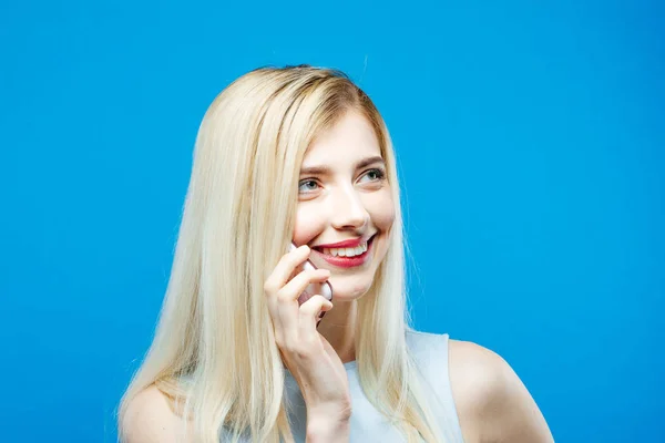 Ritratto di donna sorridente che parla tramite telefono cellulare su sfondo blu. Bionda con i capelli lunghi con Smartphone in Studio . — Foto Stock