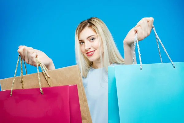 Cute Female Shopper Wearing Dress is Holding Shopping Bags on Blue Background. Happy Girl with Lond Hair and Charming Smile in Studio.