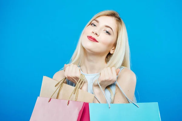 Smiling Satisfied Woman Holding a lot of Shopping Colorful Bags in Studio. Счастливая блондинка с Лонд Хайр и обаятельной Смиль на голубом фоне . — стоковое фото