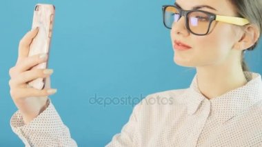 Tatlı esmer alarak Selfie Studio mavi arka plan Smartphone'da tarafından portresi. Çekici Hipster kız moda gözlük ve onun hareket eden fotoğraf çekme kendisi için kullanma.