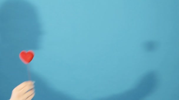 女の子シルエット スタジオで青の背景に赤の小さな心を保持している女性の手. — ストック動画