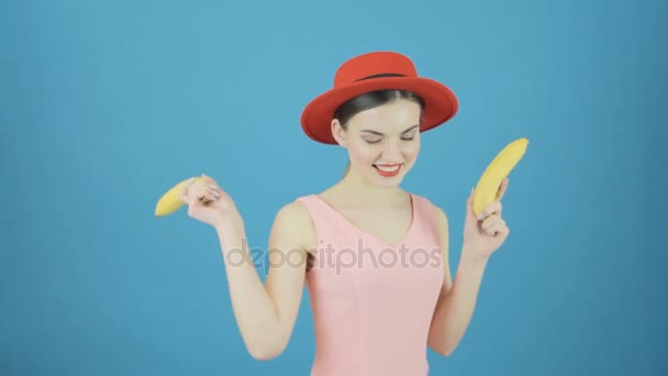 Funny Brunette Girl with Red Hat and Two Bananas is Dancing on Blue Background in Studio. — Stock Video