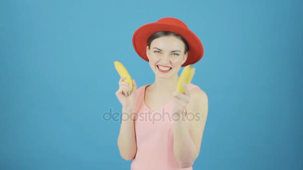 Retrato de mulher de cabelos escuros engraçado com chapéu vermelho e duas bananas está se divertindo no fundo azul no estúdio . — Vídeo de Stock