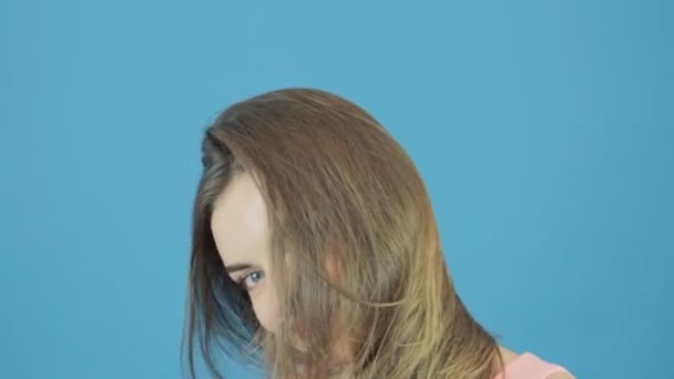 Gros plan portrait de belle femme aux longs cheveux foncés, robe rose et charmant sourire posant en studio sur fond bleu . — Video