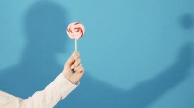 Kız gölge Studio ile mavi arka plan üzerinde renkli lolipop tutan el.