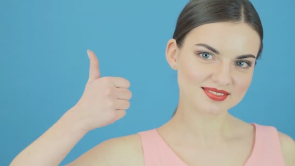 Amazing Woman está mostrando pulgares en fondo azul en el estudio. Hermosa morena gesticula mirando a la cámara . — Vídeo de stock