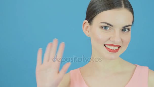 Pretty Woman Says Hello Using Hand on Blue Background in Studio. Beautiful Brunette Gesticulates Looking at the Camera. — Stock Video