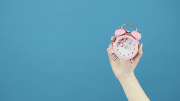 Reloj rosa con la mano femenina sobre fondo azul en el estudio . — Vídeo de stock