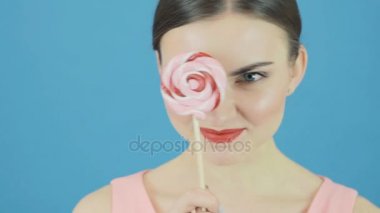 Güzel esmer şeker ile Studio poz. Büyük tatlı lolipop mavi arka plan üzerinde el ile oynak şirin kız.