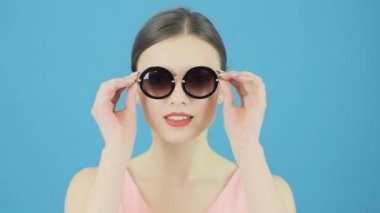 Esmer modeli Fashional güneş gözlüğü takıyor ve mavi arka plan üzerinde pembe elbiseli Güzellik Portresi. Posing Studio mükemmel kızdır.