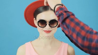 Sırasında profesyonel esmer Model Photoset. Erkek el bir şapka değişiyor. Kırmızı şapka ve pembe elbise şehvetli dudakları ile seksi kadın moda portre.