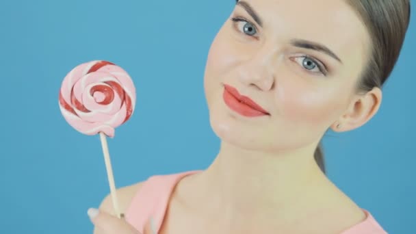 Amazing Brunette poseren in Studio met snoep. Grappig meisje met grote zoete lolly in de Hand op blauwe achtergrond. — Stockvideo