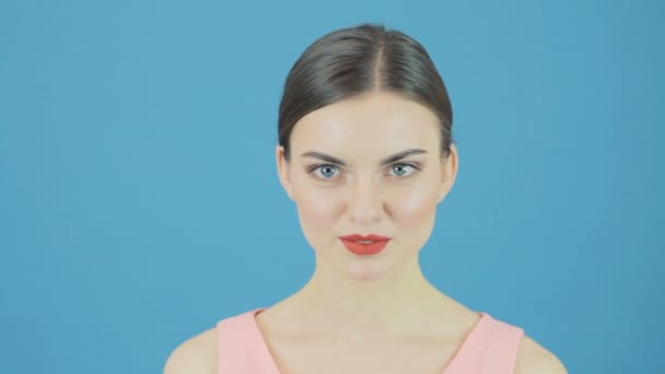 Brünette versteckt ihr Gesicht mit rotem Hut auf blauem Hintergrund im Studio. — Stockvideo