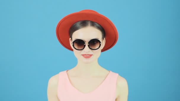 Studio mavi arka plan üzerinde kırmızı şapka ve pembe elbise giyen kadın portresi. — Stok video