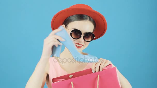 Femmina Shopper indossare cappello rosso e occhiali da sole è in possesso di borse della spesa e scarpe blu. Concetto di vendita stagionale . — Video Stock