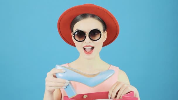 Happy Female Shopper con sombrero rojo y gafas de sol es la celebración de bolsas de compras y zapatos azules. Concepto de venta estacional . — Vídeo de stock