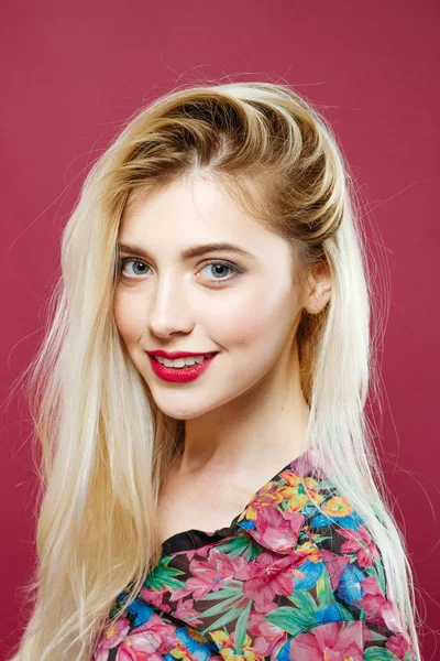 Portret van verbazingwekkende Blonde met lange haren kijken naar de Camera en glimlachend op roze achtergrond in de Studio. — Stockfoto