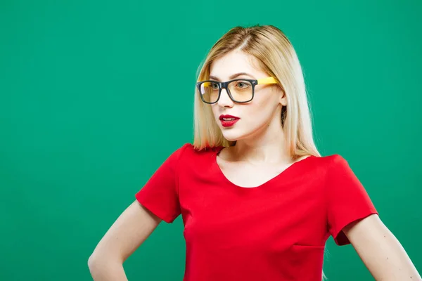 Primo piano Ritratto di ragazza sorpresa che indossa Top rosso corto e occhiali da vista. Sensuale bella bionda con i capelli lunghi è in posa su sfondo verde in studio . — Foto Stock