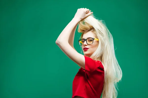 Vue latérale d'une incroyable blonde aux cheveux longs et aux lunettes posant sur fond vert en studio . — Photo