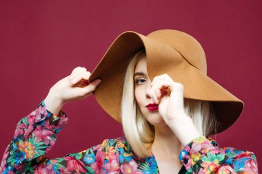 Sarışın Model kapsayan bir şık şapka tarafından gözdür. Posing Studio pembe arka plan üzerinde renkli gömlek güzel kadındır.