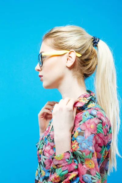 Vue latérale de jolie fille avec queue de cheval portant chemise colorée et lunettes de vue sur fond bleu en studio . — Photo