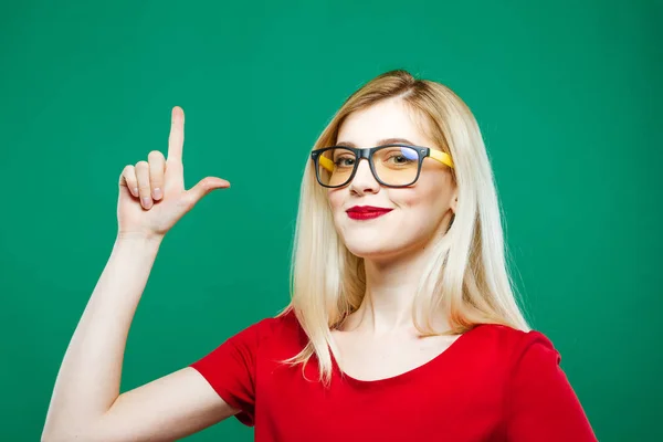 Carino Bionda si presenta da Finger e Sorridente su sfondo verde. Ritratto di Bella Ragazza in Studio . — Foto Stock